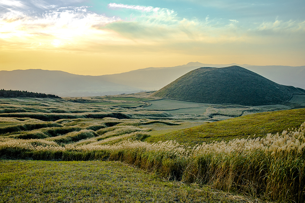 An amazing view of Mount Aso in Japan which is surrounded by golden grasslands during the sunset.